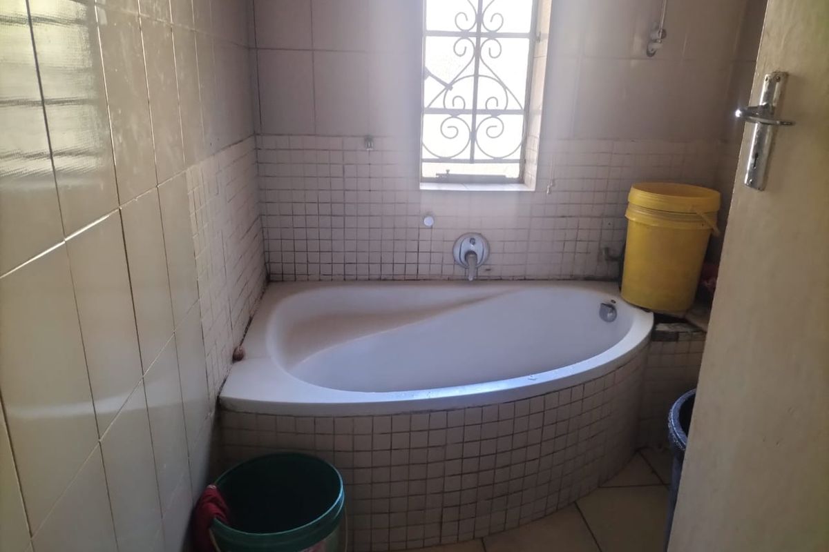 A compact bathroom featuring a built-in corner bathtub with tiled surround and flooring, requiring some maintenance and cosmetic updates.