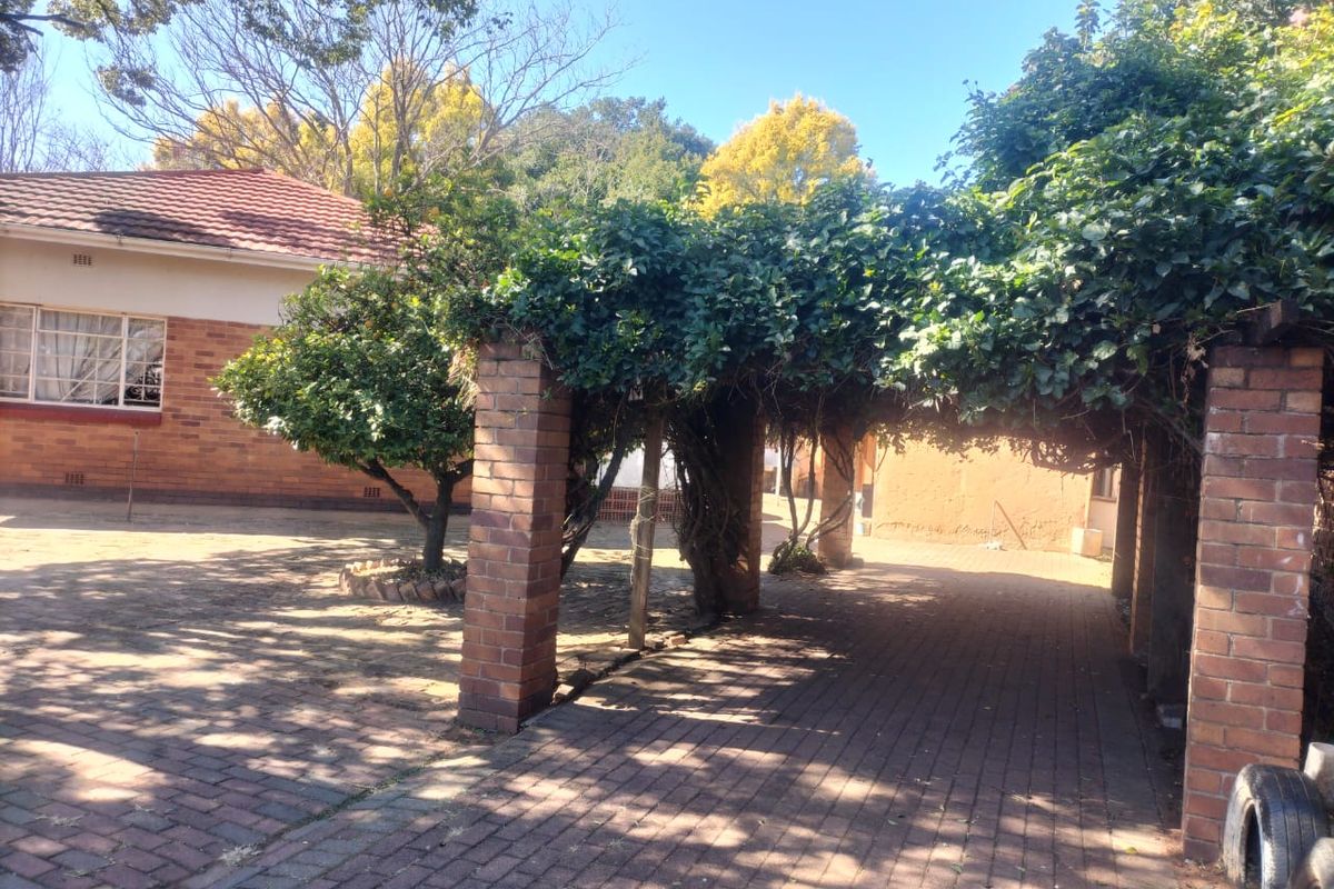 Rear exterior view featuring a brick-paved courtyard, a covered pergola structure with established climbing plants, and a face brick house facade.