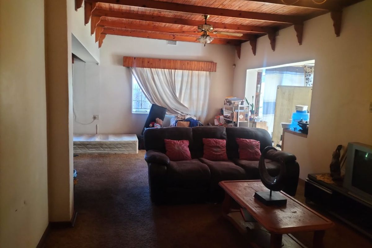 A living room featuring exposed timber ceiling beams, a ceiling fan, and carpeted flooring, offering a dated aesthetic with potential for modernization.
