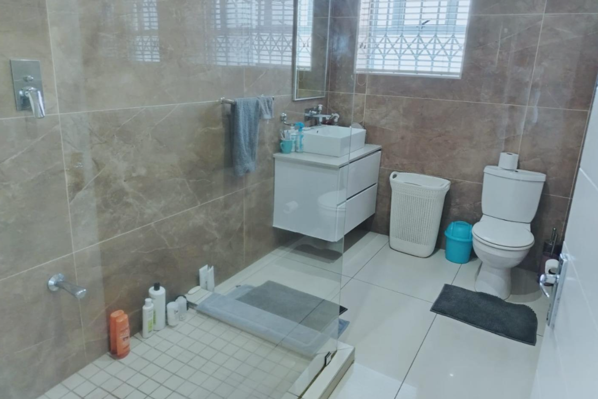 Modern bathroom featuring a wall-mounted vanity with vessel sink, glass shower enclosure, and neutral floor-to-ceiling tiling.