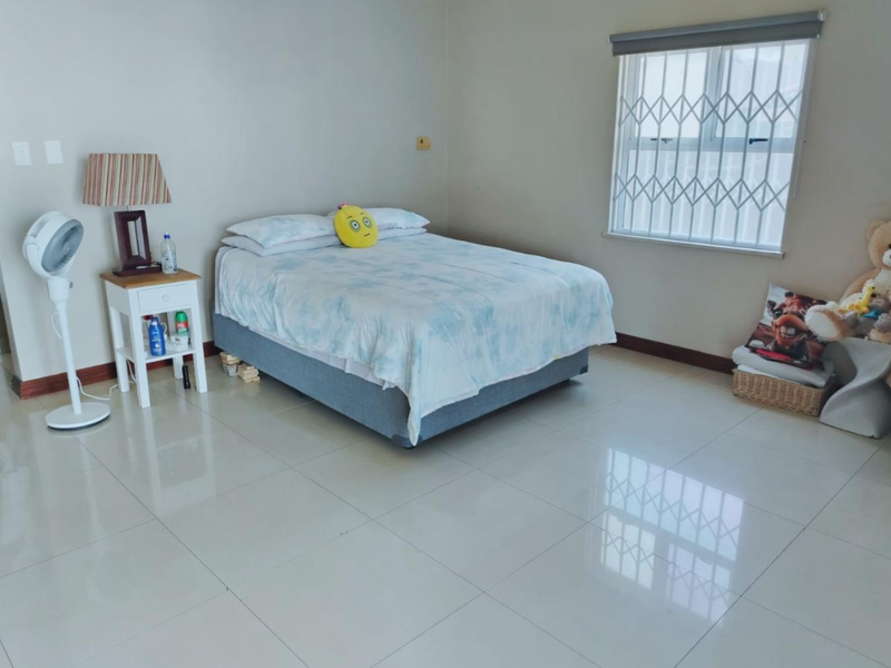 A spacious bedroom featuring polished tile flooring, neutral wall finishes, and a window fitted with a security gate.