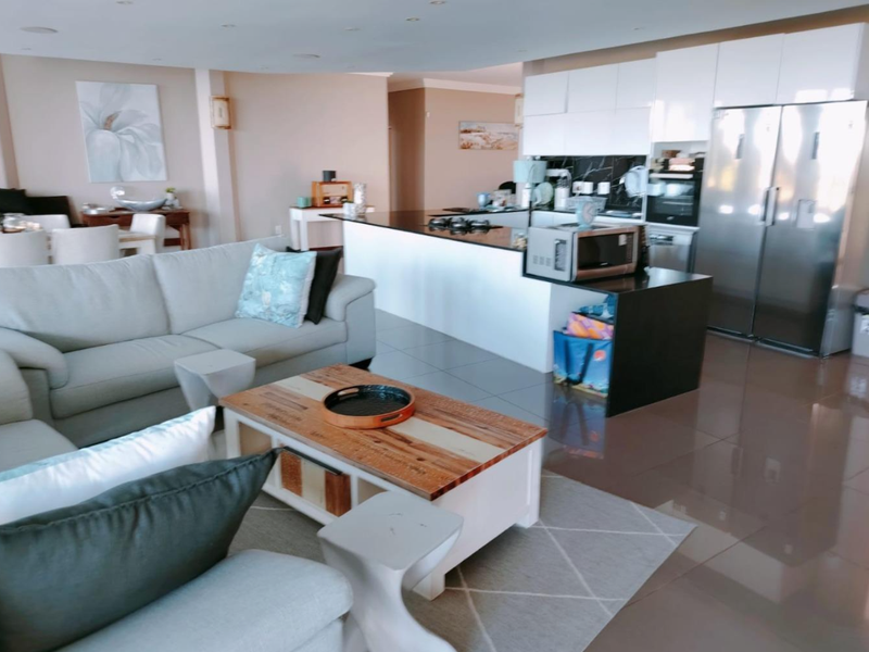Spacious open-plan living area featuring a modern kitchen with stone countertops, integrated appliances, and sleek cabinetry, seamlessly flowing into the lounge space.