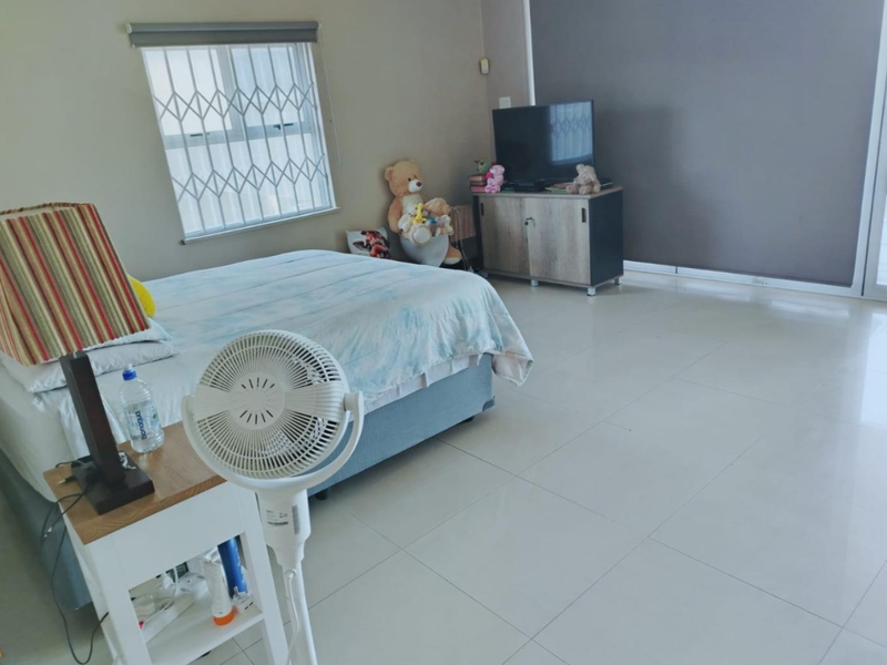 Spacious bedroom featuring neutral tiled flooring, a window with security gate, and a sliding door providing access to the exterior.
