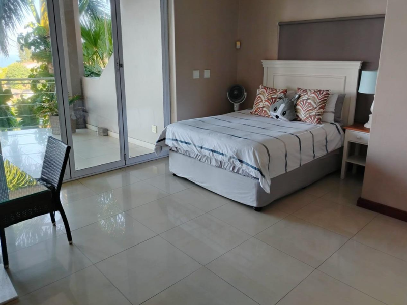 Spacious bedroom featuring large sliding glass doors that open onto a private balcony, providing ample natural light and tiled flooring throughout.