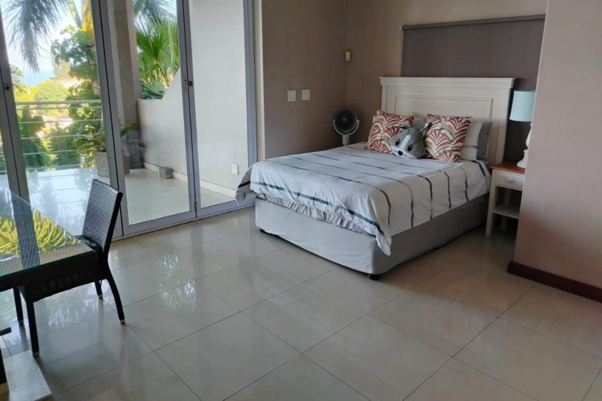 Spacious bedroom featuring large sliding glass doors that open onto a private balcony, providing ample natural light and tiled flooring throughout.