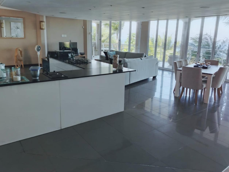 Spacious open-plan living and kitchen area featuring a modern kitchen island with gas hob, large format tiling, and expansive floor-to-ceiling glass doors.