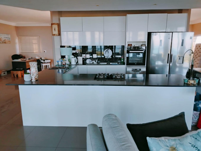 Modern open-plan kitchen featuring sleek white cabinetry, dark stone countertops, a built-in gas hob, and an integrated oven, seamlessly flowing into the living area.