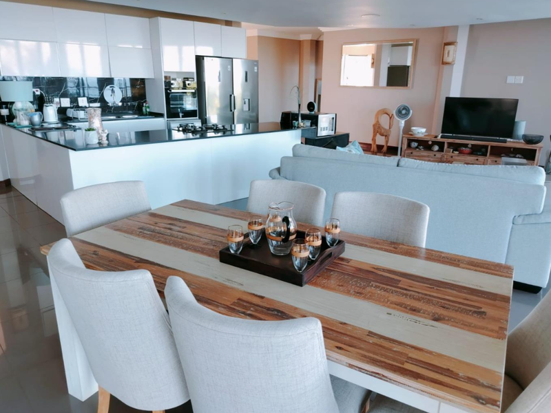 Spacious open-plan living area featuring a modern kitchen with white cabinetry, stone countertops, and integrated appliances, seamlessly flowing into the dining and lounge space.