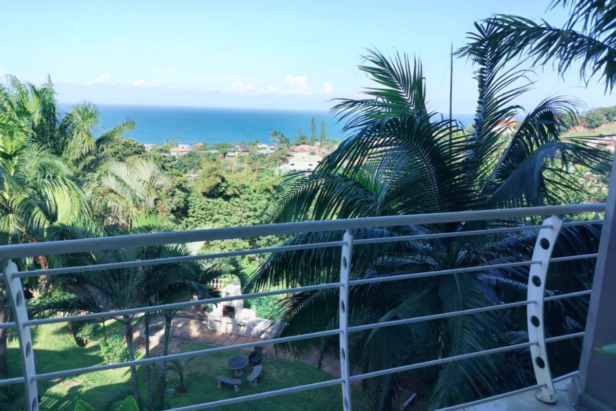 Elevated balcony view overlooking lush tropical gardens and the distant ocean coastline.