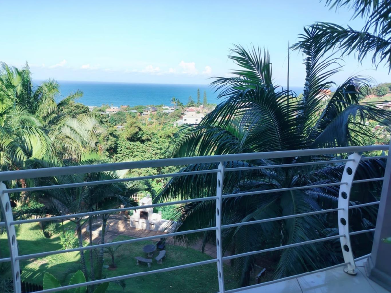 Elevated balcony view overlooking lush tropical gardens and the distant ocean coastline.