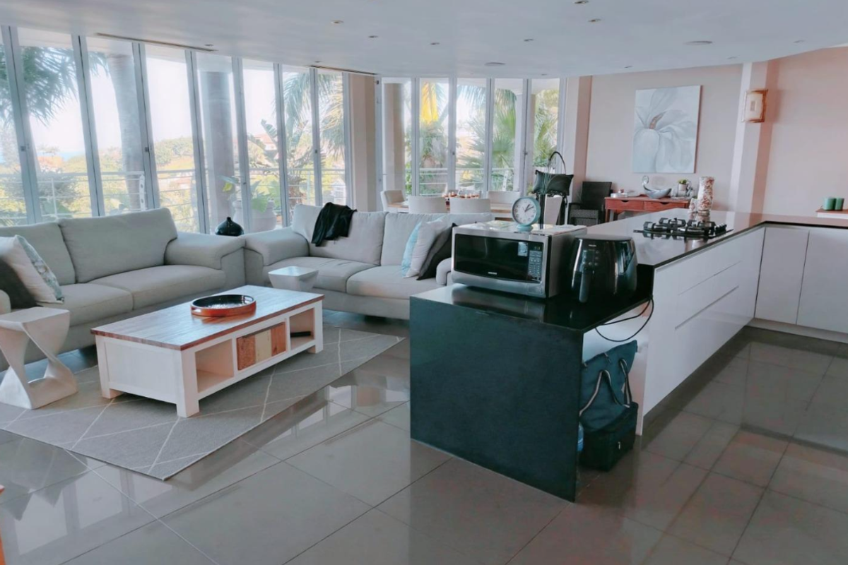 Spacious open-plan living area featuring a modern kitchen with a large island, gas hob, and expansive floor-to-ceiling windows providing natural light.