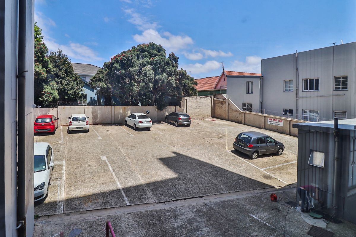 An elevated view of a paved outdoor parking area located at the rear of the apartment building, featuring a perimeter boundary wall.