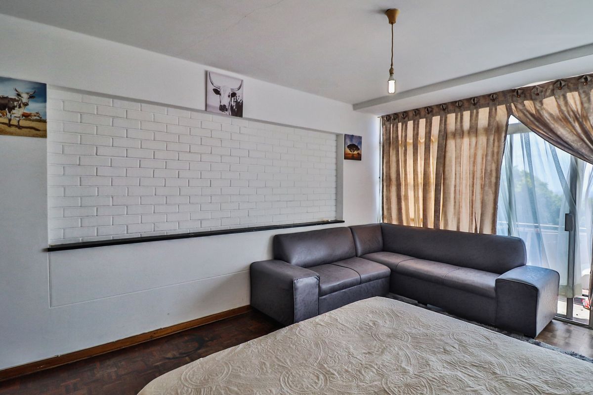 Living room featuring a white exposed brick accent wall, dark parquet flooring, and a sliding glass door providing access to the balcony.