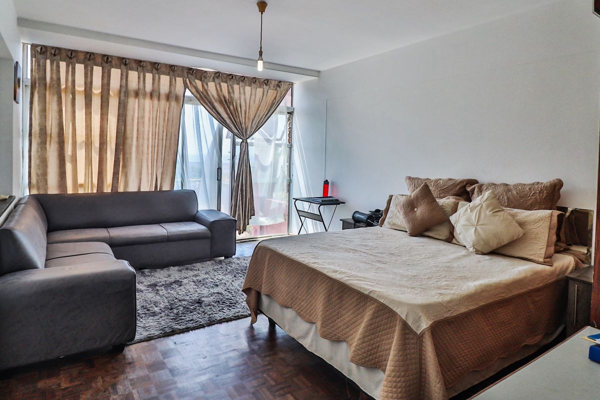 Spacious bedroom featuring parquet flooring, an exposed brick accent wall, and large sliding glass doors providing access to the balcony.