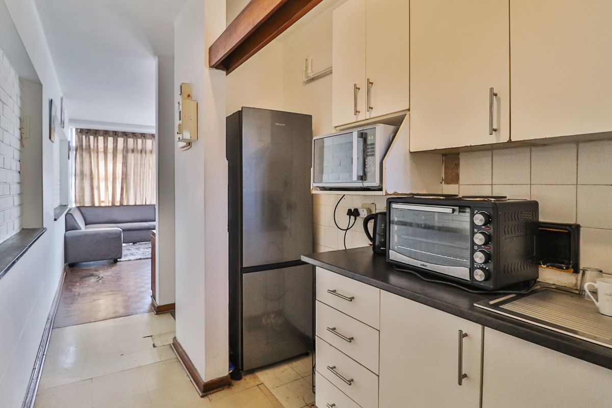 Compact kitchen area featuring built-in cabinetry, laminate countertops, and tiled backsplash, leading into an adjacent living space.