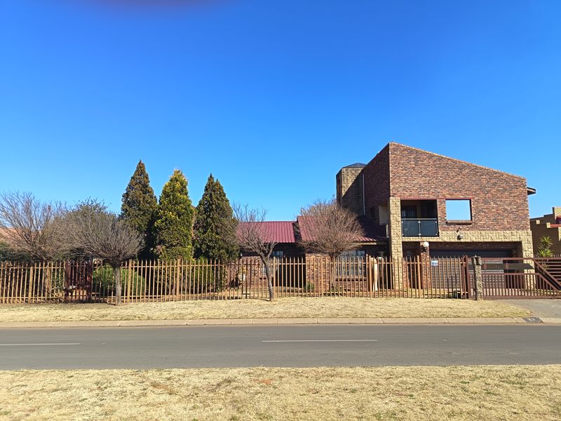 Front elevation of a multi-level face brick house featuring a metal roof, secure perimeter fencing, and an upper-level balcony.
