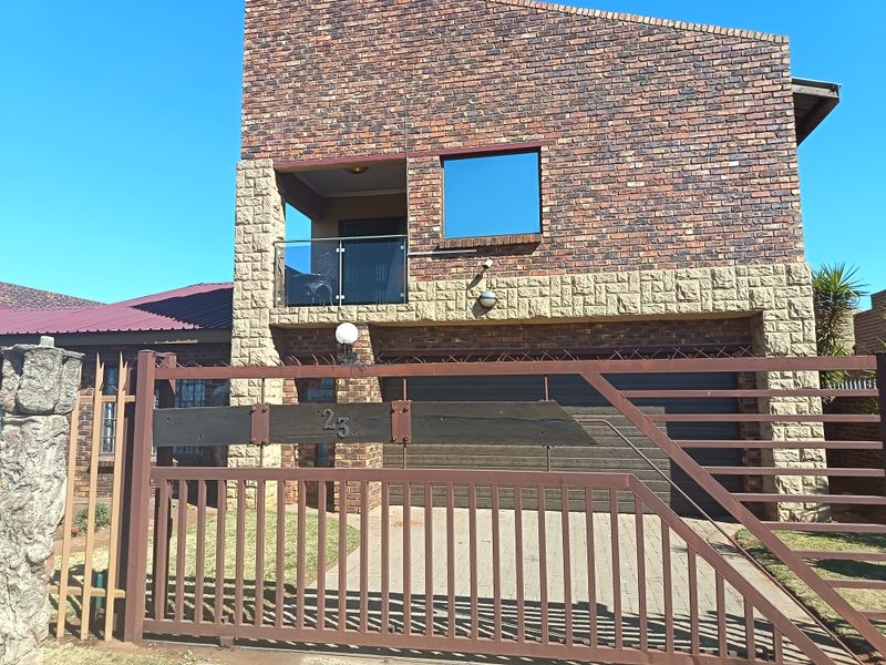 Front elevation of a double-story face brick house featuring stone cladding, a balcony with glass balustrade, and a secure metal gate entrance.