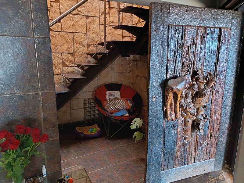 A unique hallway featuring a floating staircase with stainless steel handrails, rustic stone wall cladding, and a distinctive custom-carved timber door.