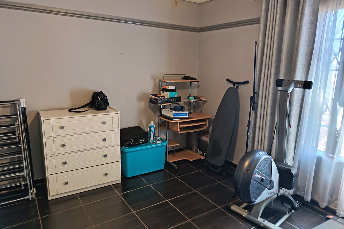 A bedroom featuring dark floor tiles and neutral wall paint with a picture rail, currently utilized as a multi-purpose storage and exercise space.