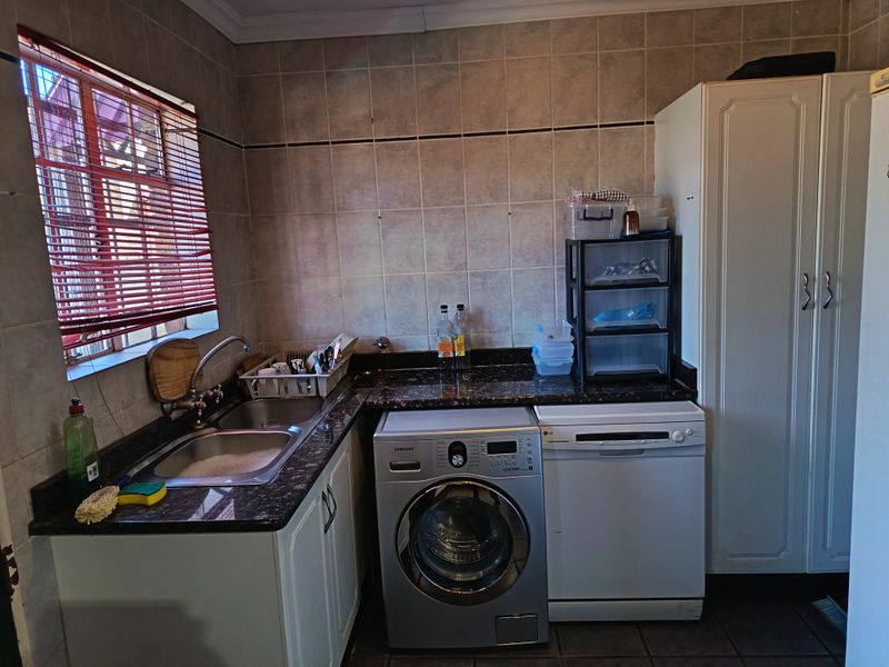 Functional laundry area featuring granite countertops, stainless steel sink, and built-in cabinetry with space for under-counter appliances.