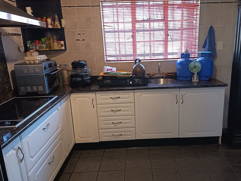 A functional kitchen featuring white cabinetry, dark countertops, tiled backsplash, and ceramic floor tiles, providing a practical workspace with integrated storage and sink.