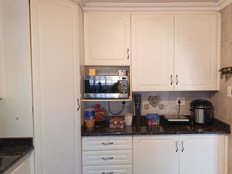 A functional kitchen area featuring white cabinetry, dark granite countertops, a tiled backsplash, and a built-in microwave unit.