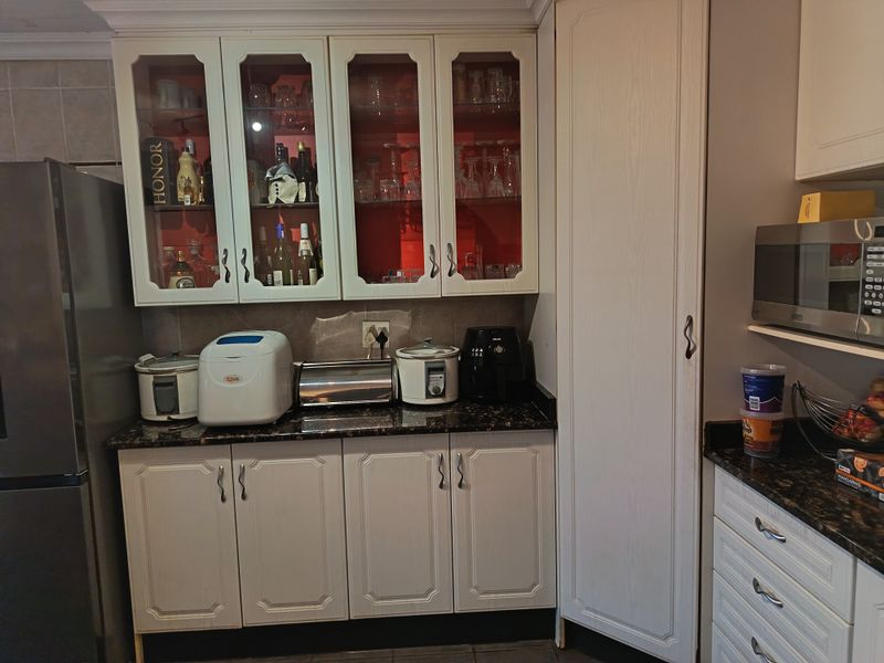 A functional kitchen area featuring white cabinetry, granite countertops, glass-front display cupboards, and a built-in microwave.