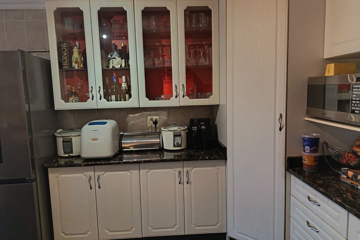 A functional kitchen area featuring white cabinetry, granite countertops, glass-front display cupboards, and a built-in microwave.