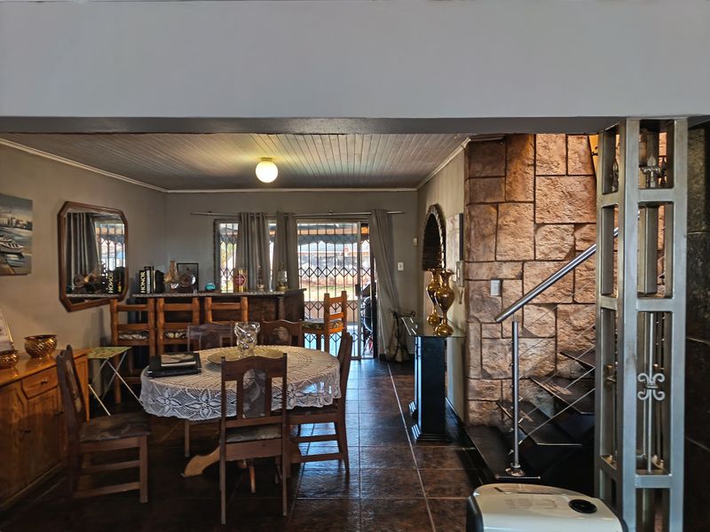 Open plan living and dining area featuring a stone-clad feature wall, staircase with metal balustrade, and direct access to the outdoor area via sliding doors.
