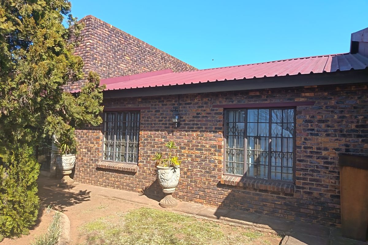 A view of the rear exterior featuring face brick walls, a corrugated metal roof, and windows fitted with security bars.