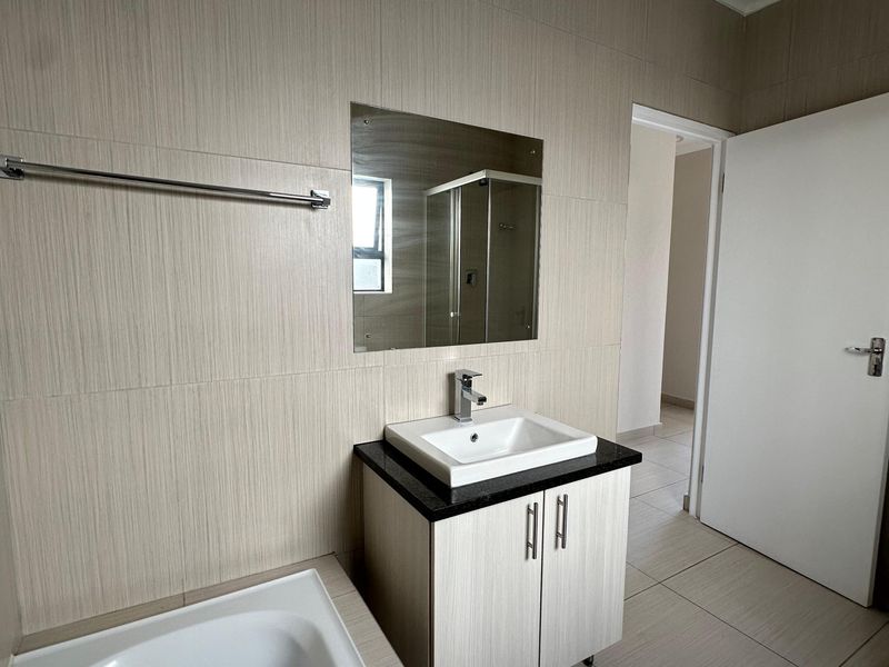 A clean, modern bathroom featuring a vanity with a basin, a bathtub, and neutral wall and floor tiling.