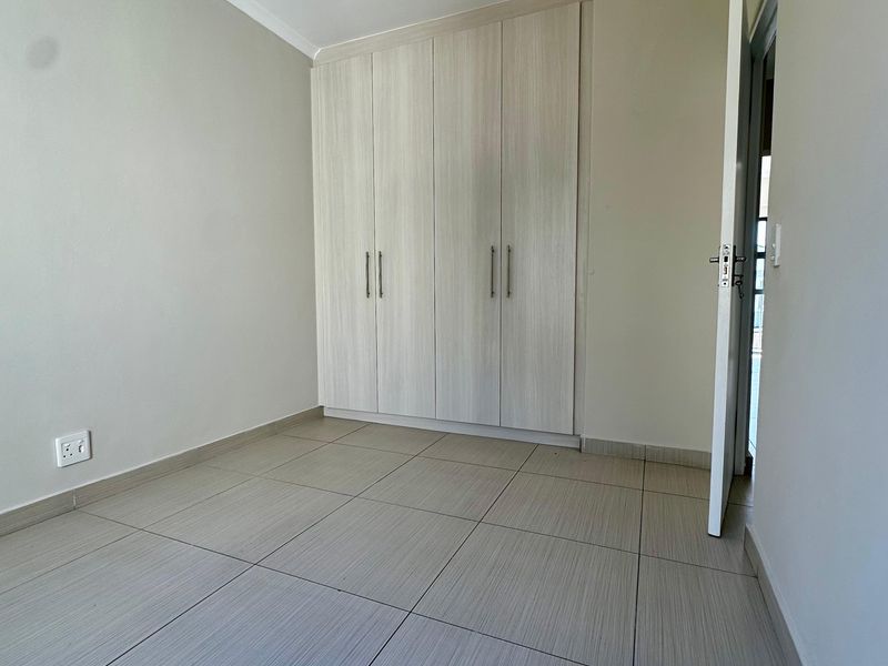 A clean, empty bedroom featuring neutral tiled flooring, built-in cupboards with light wood-grain finish, and coved ceiling detailing.