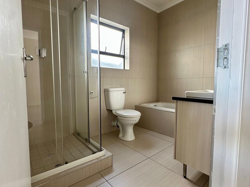 A clean, modern bathroom featuring a glass-enclosed shower, a built-in bathtub, and a vanity cabinet with neutral floor-to-ceiling tiling.