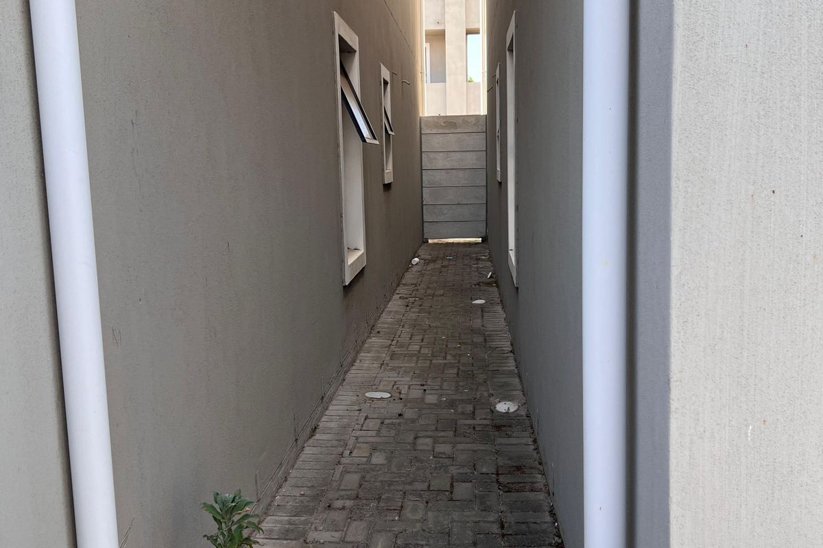 A narrow side passage between townhouse units featuring paved flooring and external drainage downpipes.