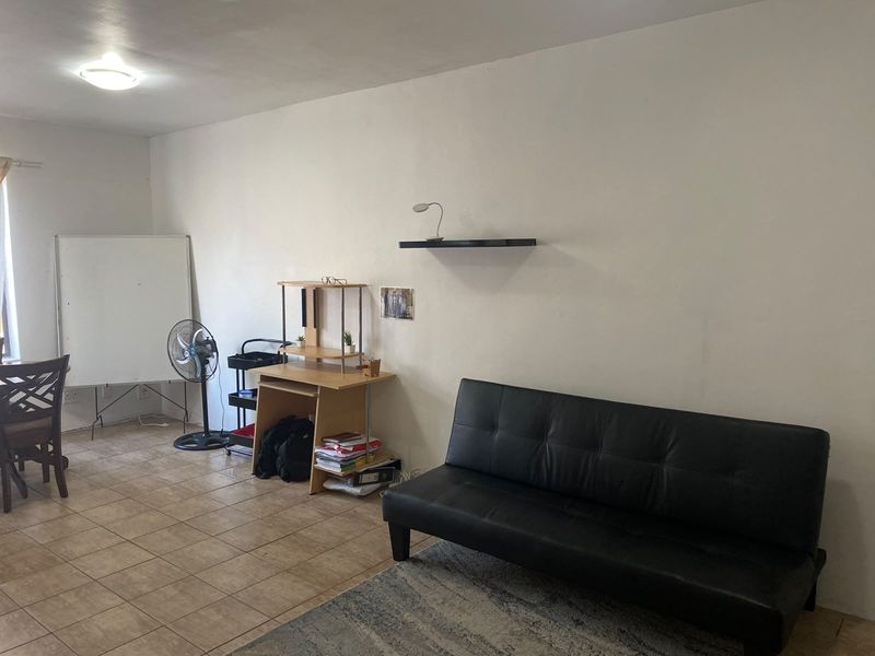 A living area featuring tiled flooring and a wall-mounted shelf, providing a functional space with neutral finishes.