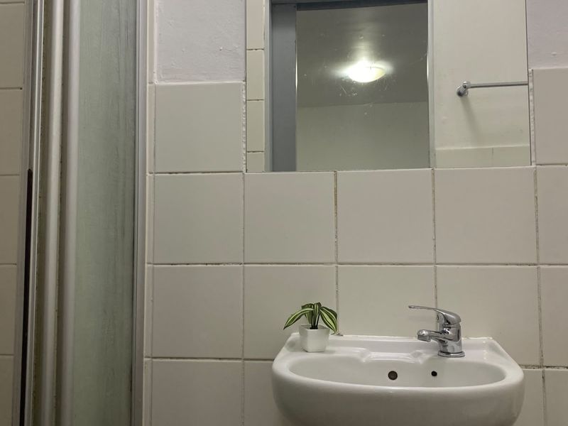 A compact bathroom featuring a wall-mounted basin with chrome mixer tap, tiled splashback, and a shower enclosure.