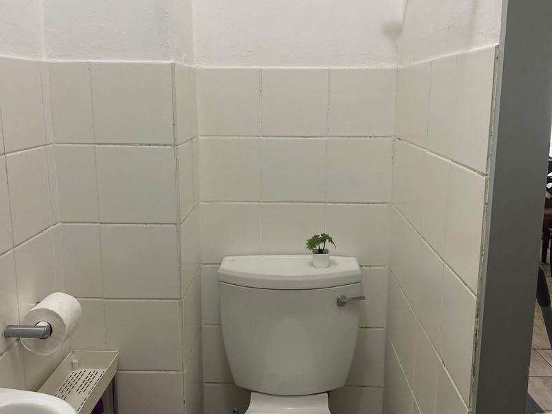 A compact bathroom featuring a standard toilet, wall-mounted washbasin, and white ceramic wall tiling.