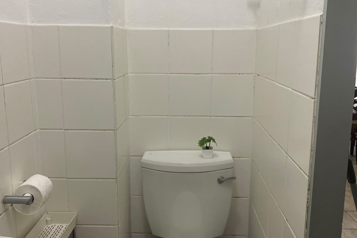 A compact bathroom featuring a standard toilet, wall-mounted washbasin, and white ceramic wall tiling.