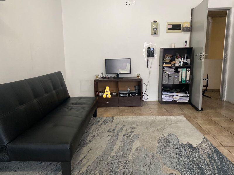 A living room area featuring tiled flooring, wall-mounted intercom system, and electrical distribution board, requiring cosmetic updates to improve the overall aesthetic.