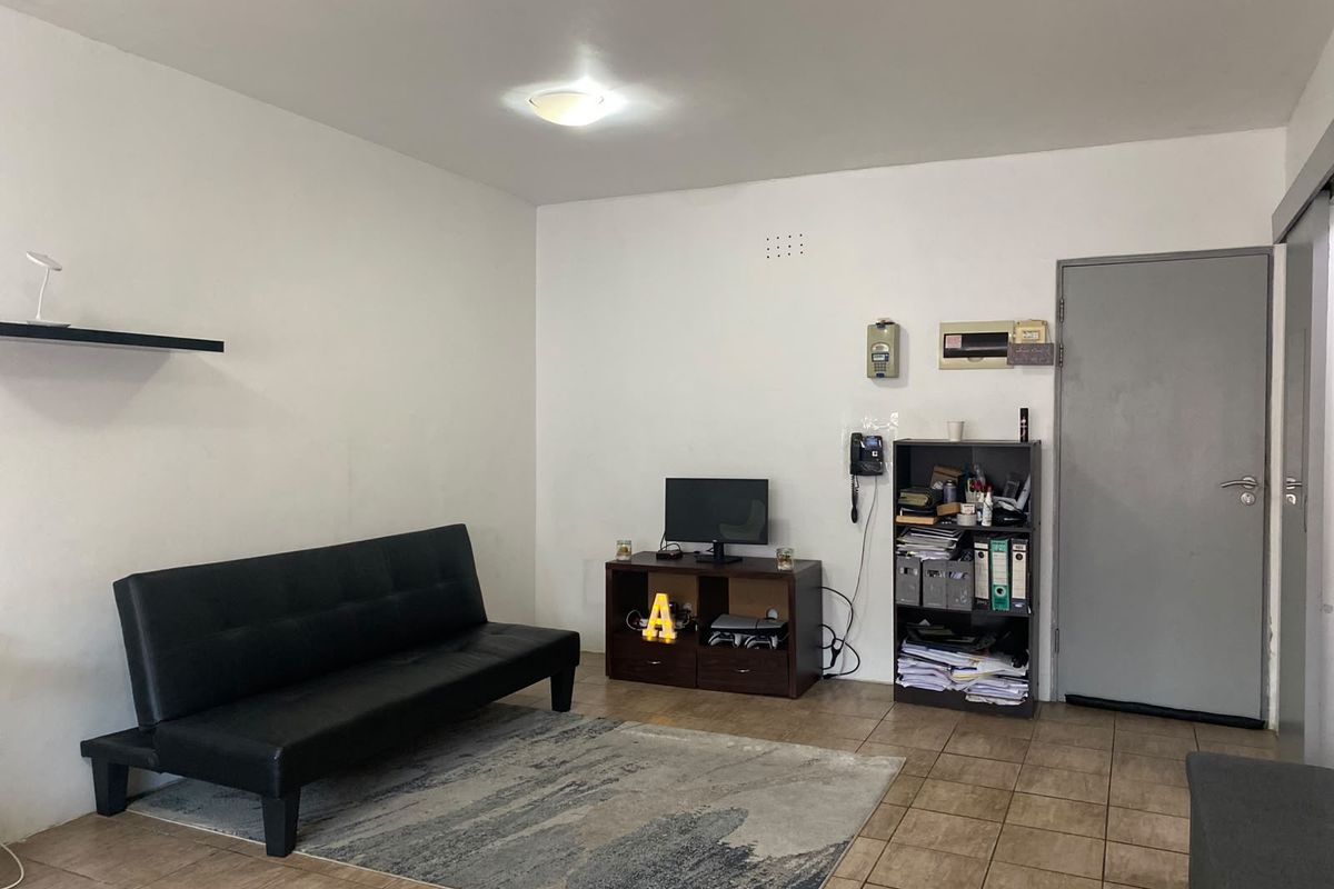 A functional living room featuring tiled flooring, an intercom system, and a neutral wall finish, providing a blank canvas for interior design updates.