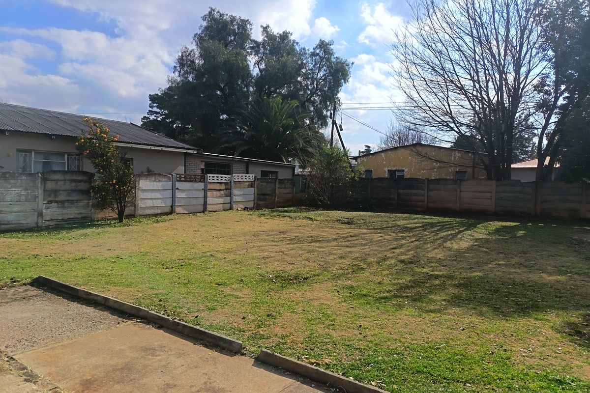 A spacious rear garden area featuring a large lawn, concrete driveway, and perimeter precast concrete boundary walls.
