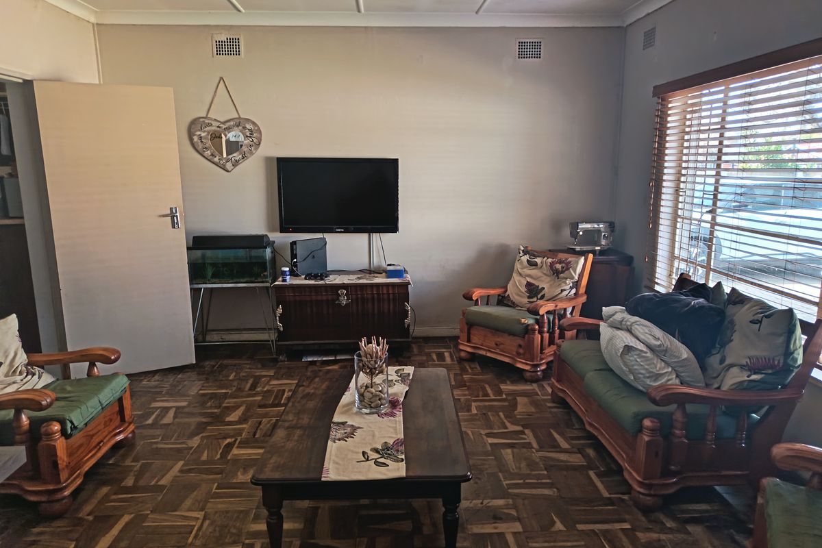 A living room featuring traditional parquet flooring, timber window blinds, and neutral wall finishes, offering a functional space with potential for cosmetic updates.