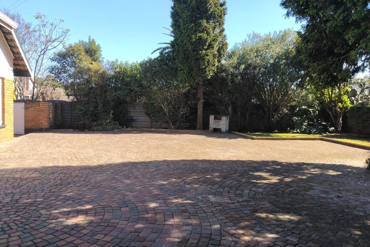 A spacious rear courtyard featuring extensive brick paving, a built-in braai, and established garden borders.