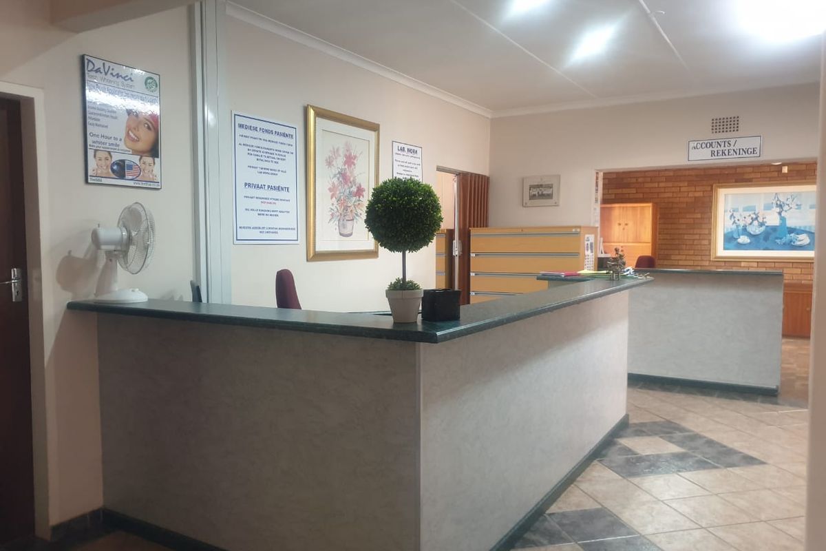 A commercial reception area featuring a built-in service counter, tiled flooring, and a drop ceiling, currently configured for office or medical administrative use.