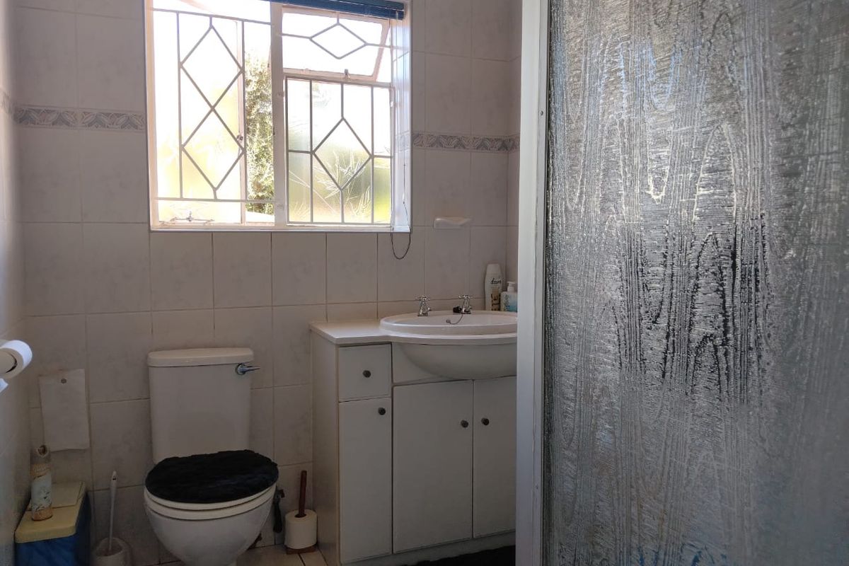 A functional bathroom featuring a vanity cabinet with basin, toilet, and a shower enclosure with textured glass door.