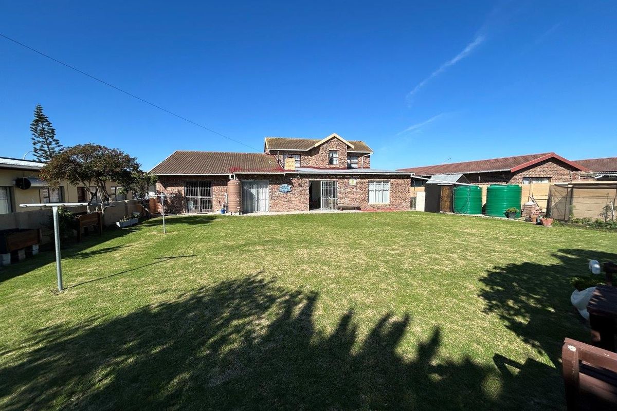 Rear view of a double-story brick house featuring a spacious lawn, security gates, and external water storage tanks.