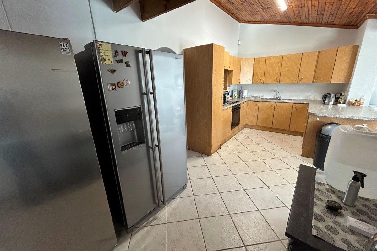 Functional kitchen featuring wooden cabinetry, laminate countertops, tiled flooring, and exposed timber ceiling beams, offering a practical layout for daily use.