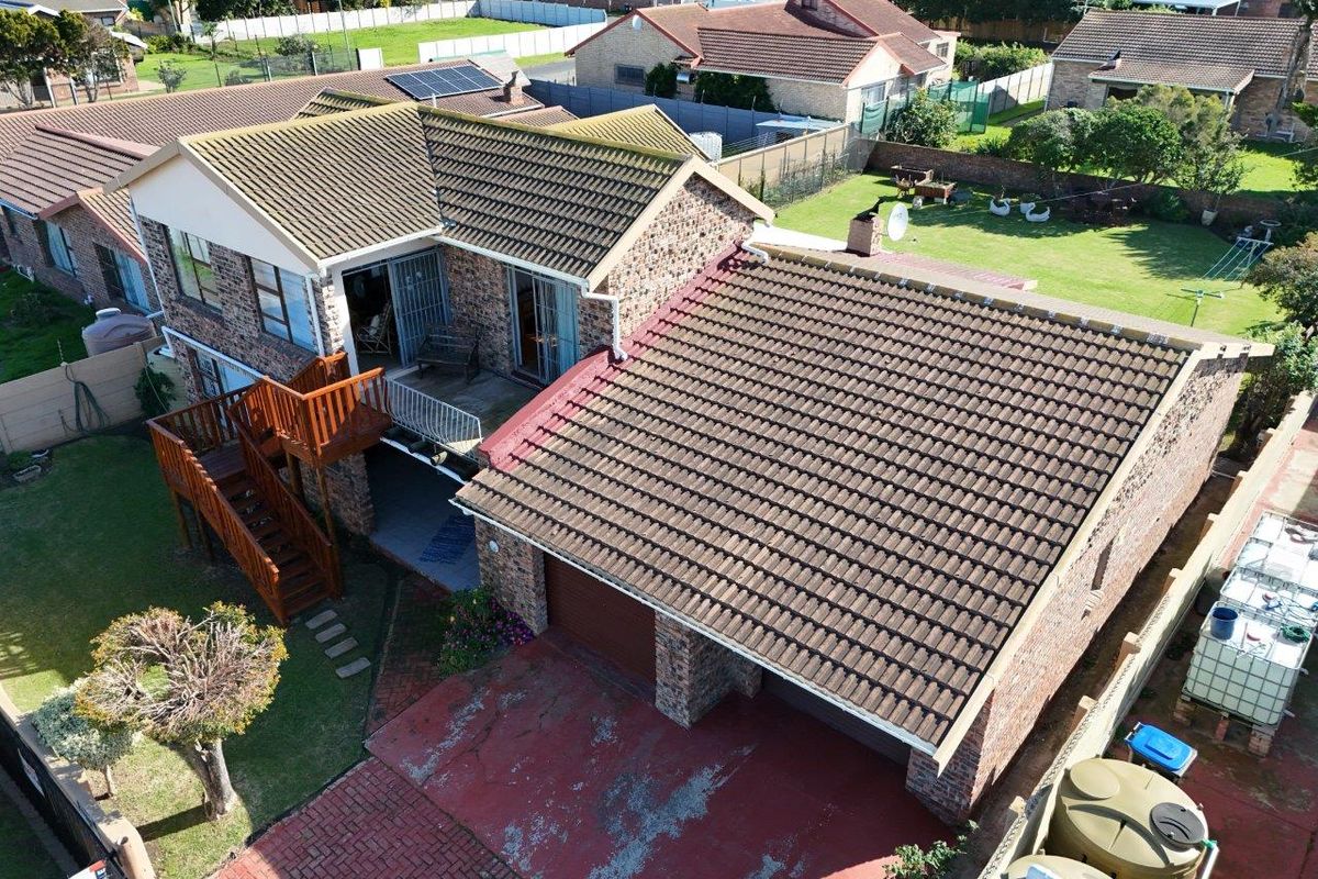Aerial view of a brick-faced residential property featuring a tiled roof, double garage, wooden staircase, and a spacious garden with water storage tanks.