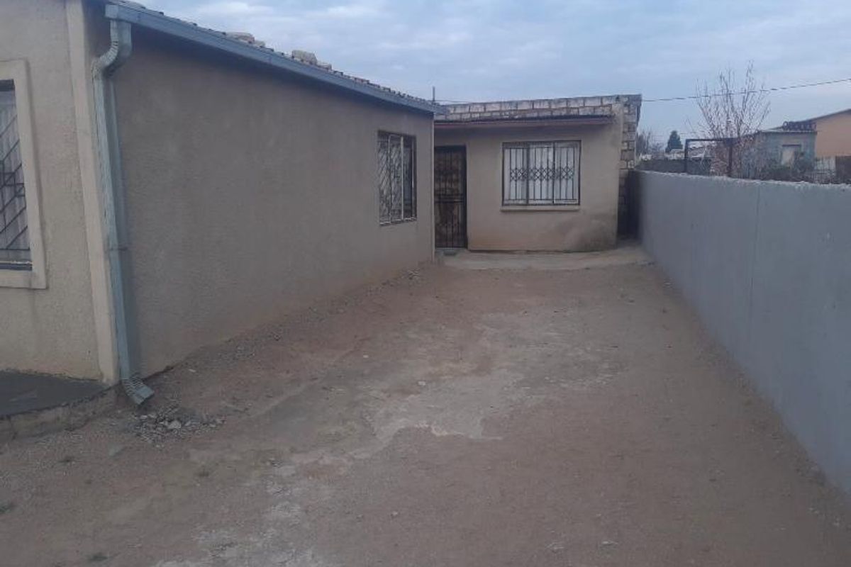 Rear exterior view of the property featuring a concrete yard area, boundary wall, and security bars on windows.