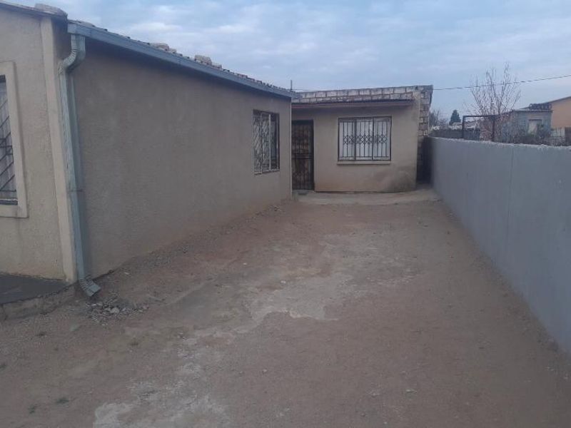Rear exterior view of the property featuring a concrete yard area, boundary wall, and security bars on windows.